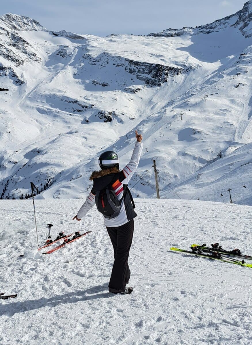 Anne Vierling auf der Skipiste vor verschneiten Berggipfeln, den Arm in die Höhe gestreckt